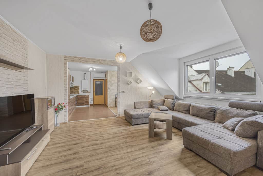 Moderní obývací pokoj s velkým gaučem a velkými okny, ideální pro relaxaci.