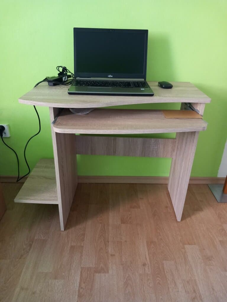 Počítačový stůl s monitorem, klávesnicí a myší v domácím prostředí.