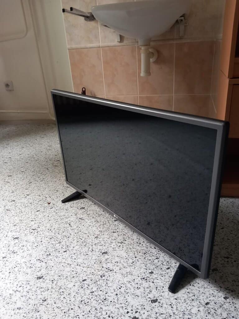 Televize s černým displejem stojí na podlaze v koupelně.