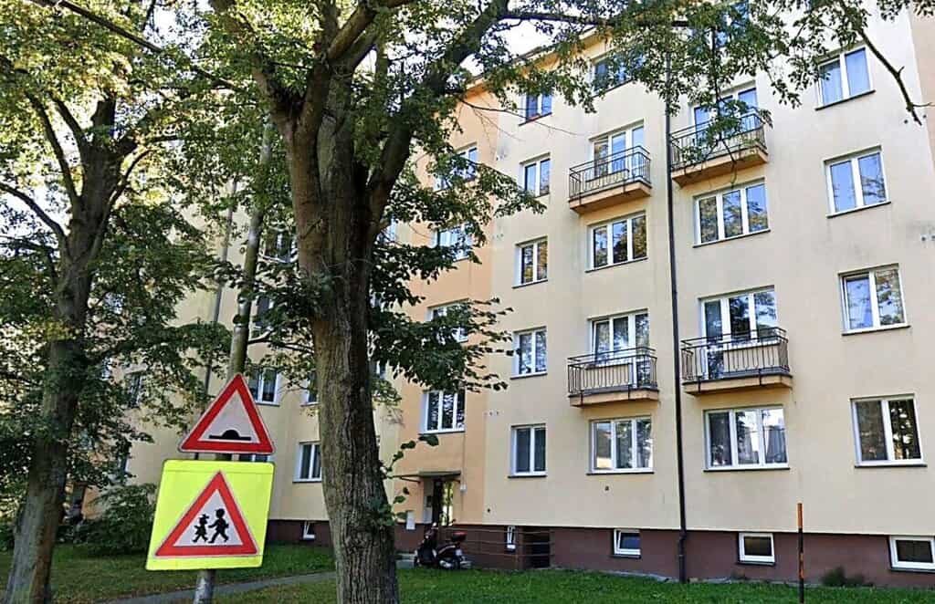 Panelový dům s několika balkony a okolní zelení.