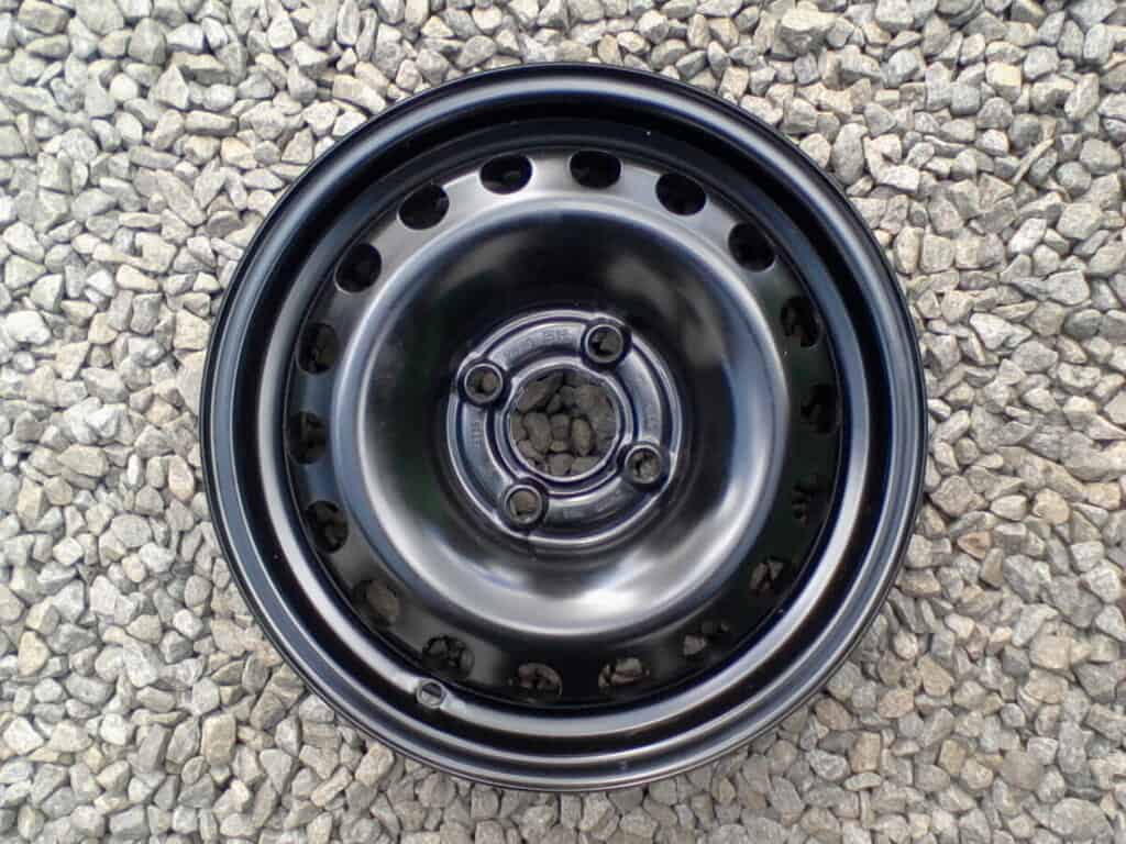 Černé hliníkové kolo na šedém štěrku, vhodné pro osobní automobil.