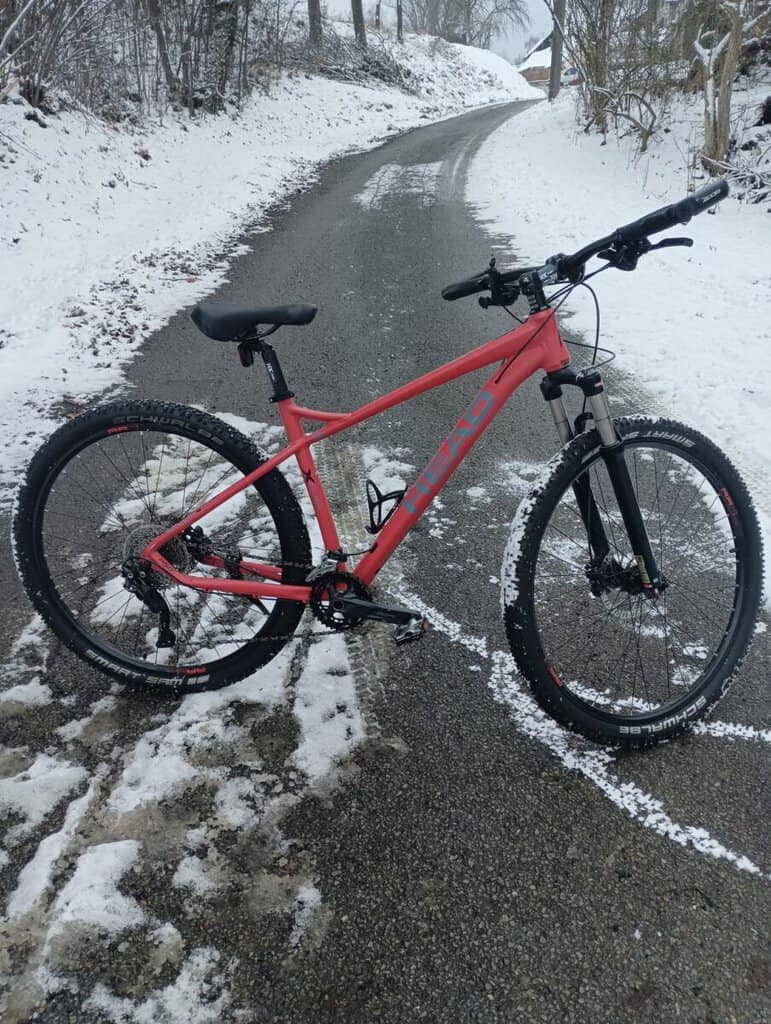 Horské kolo růžové barvy na zasněžené cestě.