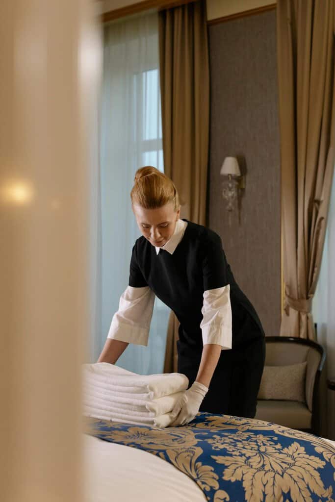 Číšnice skládá ručníky na hotelové posteli v elegantním pokoji.