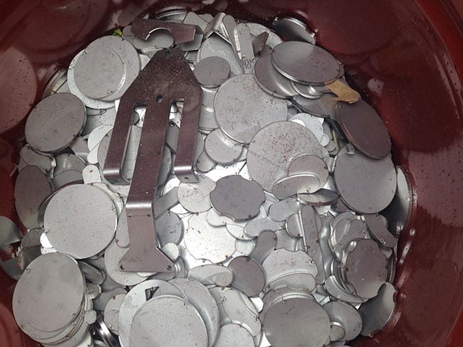 Hliníkové mince a kovové odpadky v červené nádobě, vhodné pro recyklaci a sběr kovových od.